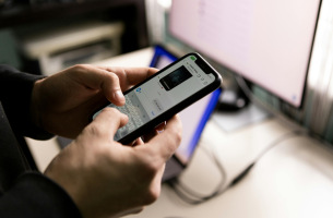 Bilde ar mobilo telefonu un fonā datoru